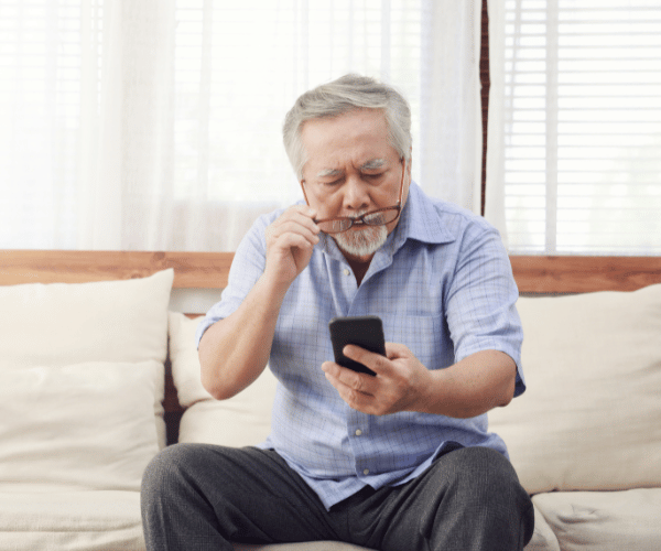 Elderly man struggling to read on his phone, showcasing symptoms of blurry vision due to cataracts.