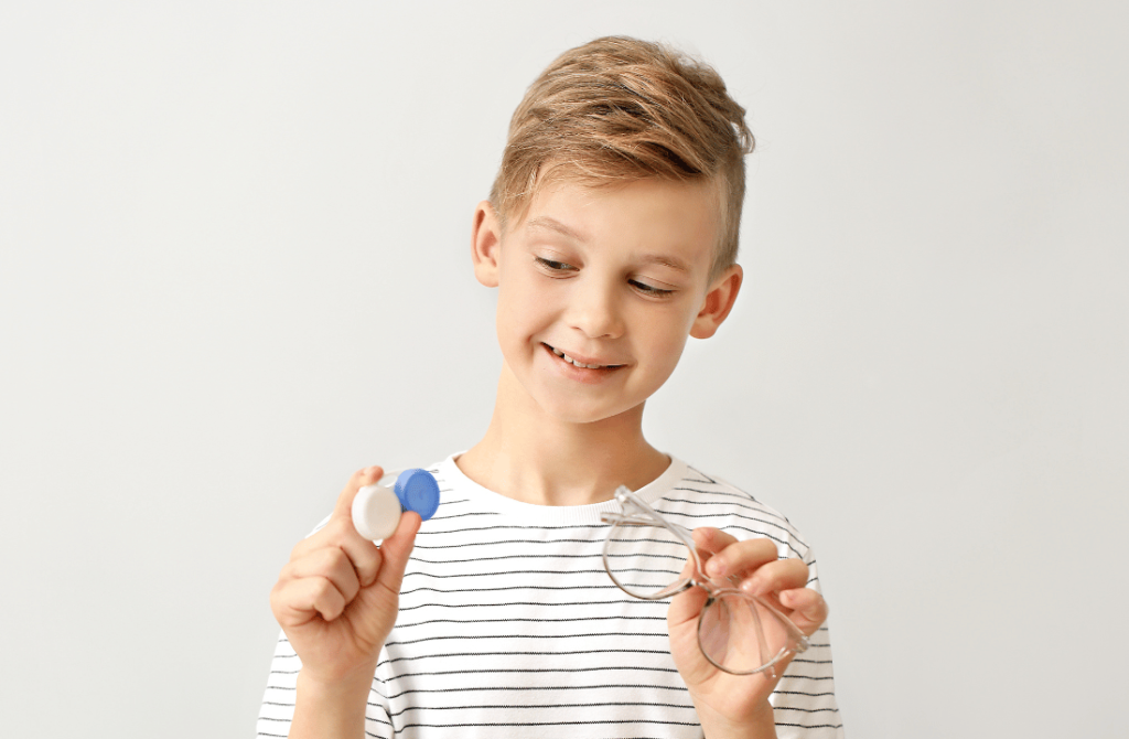 Boy holding eyeglasses or contact lenses, highlighting options for vision correction in children.