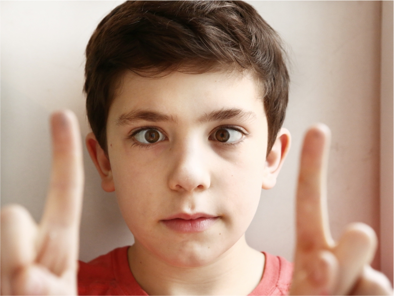 A playful boy with squint eyes peeking through his fingers, representing childhood eye conditions.